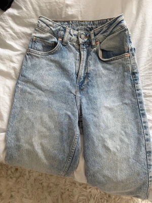 Ljusblå raka jeans med hög midja - Säljer ett par ljusblå jeans med rak passform och hög midja. Klassisk femficksmodell med knappgylf och snygg tvätt. Perfekta till en avslappnad stil och passar till det mesta. Materialet är kraftig denim i bomull.