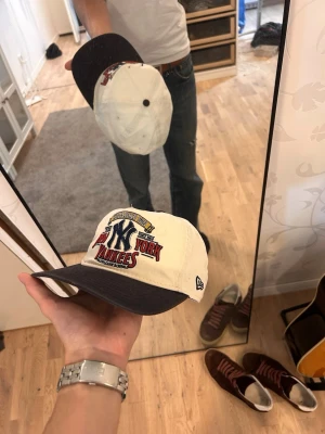 New York Yankees keps från New Era - Snygg New York Yankees keps från New Era med vit krona och mörkblå skärm. Broderad Yankees-logga och text framtill i rött, blått och gult. Klassisk 6-panels design och justerbar passform. Perfekt för dig som gillar sportig streetstyle.