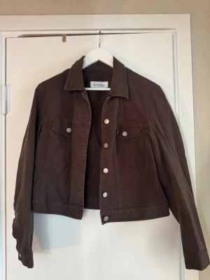 Brun jeansjacka från Intense - Snygg brun jeansjacka från Intense med klassisk krage, silverfärgade knappar och två bröstfickor med lock. Jackan har en rak passform och långa ärmar, liten i storlek.