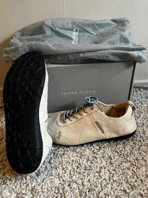 Beige mocka barfotaskor från Terra Plana - Snygga beige barfot i mocka från Terra Plana med svarta sulor och ljusgrå skosnören. Skorna har en minimalistisk design med dekorativa sömmar och låg profil. Perfekta för dig som gillar stilrena och bekväma skor.