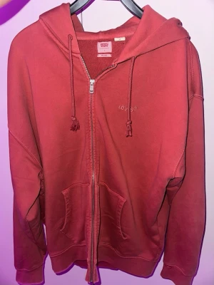 Levis tröja i storlek L  - Snygg ljusröd Levis ziphoodie i bra skick bekväm, inköpt från Levis. Säljes då den inte passar mig använd kanske 7gånger 