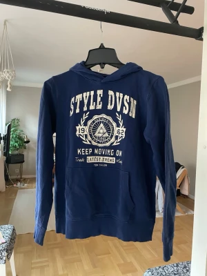 Vintage Hoodie  - Snygg mörkblå hoodie med vit text och grafiskt tryck på bröstet där det står 'STYLE DVSN' och 'Keep Moving On'. Hoodien har huva och en stor magficka framtill. Perfekt för en avslappnad vintage look. Passar XS och S och inte L som det står på tröjan!