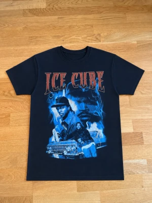 Svart Ice Cube t-shirt med tryck - Säljer en svart t-shirt med stort Ice Cube-tryck i blått och rött framtill. T-shirten har klassisk passform, rund hals och korta ärmar. Perfekt för dig som gillar streetwear och vill sticka ut med en snygg grafisk design.
