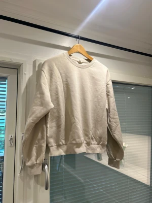 Beige oversized sweatshirt - En stilren beige sweatshirt med rund hals och ribbade muddar vid ärmslut och nederkant. Tröjan har en avslappnad, oversized passform och är tillverkad i mjukt bomullsliknande material. Perfekt för en casual look.