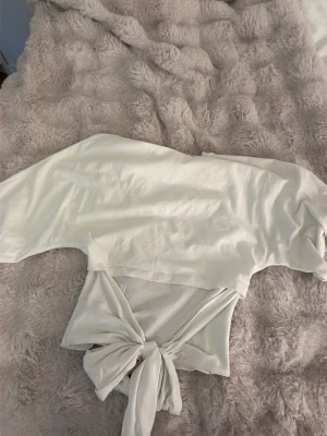 Vit croppad topp med knyt - Säljer en vit croppad topp med korta ärmar och snygg knytning i midjan. Toppen har en enkel, stilren design och är perfekt för dig som gillar trendiga detaljer. Tillverkad i mjukt bomullstyg som känns skönt mot huden.