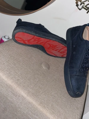 Svarta Christian Louboutin sneakers - Snygga svarta sneakers från Christian Louboutin i mocka med klassisk röd sula och diskret logga. Lågt skaft, svarta skosnören och stilren design som passar till det mesta. Perfekta för dig som gillar exklusiva detaljer och streetstyle.