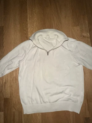 Vit tröja med halvzip - Vit stickad tröja med hög krage och halvzip framtill. Tröjan har långa ärmar och ribbade muddar vid ärmslut och nederkant. Perfekt för lager på lager och enkel att matcha med olika outfits.