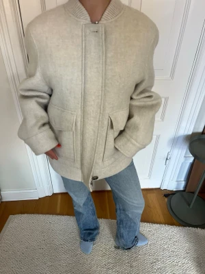 Beige oversized ulljacka - Säljer en beige oversized jacka i ull med stora fickor framtill och ribbad krage. Jackan har knappar och dragkedja för stängning samt långärmad design. Perfekt för dig som gillar en avslappnad och trendig look.