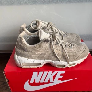 Beige Nike Air Max 95 sneakers - Snygga beige Nike Air Max 95 sneakers med ovandel i mocka och mesh. Skorna har en chunky sula med synliga Air-enheter och stänkdetaljer i vitt och beige. Klassisk Nike-logga på sidan och häl. Perfekta för dig som gillar streetwear och sportig stil. 42,5 
