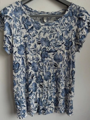 Blåblommig viskostopp med volangärm från H&M, stl S - Superfin och luftig kortärmad topp från H&M i 100% viskos. Vitt tyg med ett vackert blommigt mönster i olika blå nyanser. Toppen har en rund halsringning och jättefina, korta (flutter sleeves) som ger ett romantiskt intryck  Märke: H&M  Storlek: S (EUR S / UK S)  Material: 100% viskos  Skick: Mycket bra skick, inga defekter  Tvättråd: Maskintvätt 30 grader, stryks efter tvätt  Djur och rökfritt hem. Skickar snabbt! ✨ 