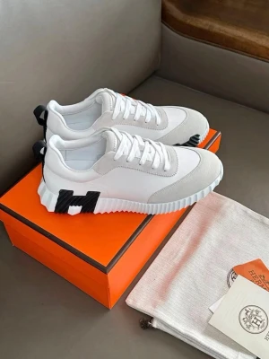 Vita sneakers med svart detalj - Stilrena vita sneakers med svart H-detalj på sidan och vit sula med räfflad kant. Ovandelen är i en mix av textil och mocka, med vita skosnören och svart hälflik. Perfekta för en trendig och avslappnad look.