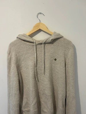 Beige hoodie från Morris Stockholm - Snygg beige hoodie från Morris Stockholm med huva och dragsko. Tillverkad i mjukt, ribbat material och har en liten broderad logga på bröstet. Perfekt för en avslappnad och stilren look.