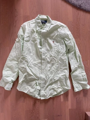 Ljusgrön skjorta från Polo Ralph Lauren - Snygg ljusgrön skjorta från Polo Ralph Lauren med klassisk button-down krage och broderad logga på bröstet. Skjortan har långa ärmar och är tillverkad i bomull för en bekväm känsla. Perfekt för en stilren och avslappnad look.
