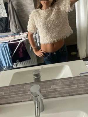 Vit fluffig croppad topp - Säljer en vit, fluffig croppad topp med korta ärmar. Toppen har en mjuk och lurvig textur som ger en cool och trendig look. Perfekt att styla med höga jeans eller kjol för en avslappnad vibe.Fluffig krämvit/beige topp från Zara 🤍 Storlek 152 cm. Kortare modell med mjukt, fluffigt material. Perfekt till Y2K, 2000s, coquette, girly och vintage-inspirerade outfits ✨