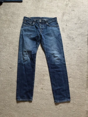 Edwin jeans - Snygga blå jeans i klassisk rak modell, tillverkade i Japan. Jeansen har fem fickor, knappgylf och subtila slitningar framtill för en avslappnad look. Perfekta för dig som gillar tidlös stil och kvalitetsdenim.