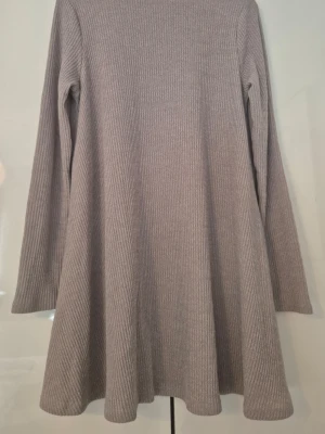 Ljusgrå ribbad klänning - En enkel och snygg ljusgrå klänning med lång ärm och rund hals. Klänningen är ribbad och har en lös passform med svängd kjol. Perfekt för dig som gillar en avslappnad men ändå stilren look.