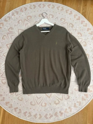 Polo Ralph Lauren V-ringad tröja - Storlek: L Färg: Mörkgrön/olivgrön Skick: Bra  Klassisk V-ringad tröja från Polo Ralph Lauren med diskret broderad polospelare på bröstet. Stilren modell med ribbade detaljer vid hals, ärmslut och nederkant.  Se bilder för skick och detaljer.