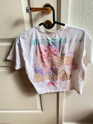 Winx Club T-shirt, Name it, 134/140 - Säljer en vit t-shirt med färgglatt anime-tryck på både fram- och baksidan. På ryggen står det 'BEST FRIENDS' och motivet visar två tecknade tjejer med pastellfärgat hår. T-shirten har rund hals och korta ärmar. Perfekt för dig som gillar anime och japansk stil.