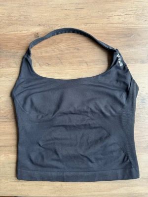 Svart halterneck linnetopp från DFYNE - Säljer en svart halterneck linnetopp från DFYNE. Toppen är ärmlös och har en sportig look med logga tryckt vid axeln. Materialet känns stretchigt och passar perfekt till träning eller som ett snyggt basplagg.