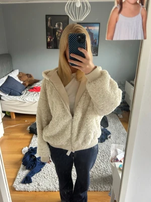 Beige teddyjacka med huva - Mysig beige teddyjacka med dragkedja och huva. Jackan har ribbade muddar vid ärmslut och nederkant samt en avslappnad passform. Perfekt för att hålla sig varm och se stylish ut under kyliga dagar.
