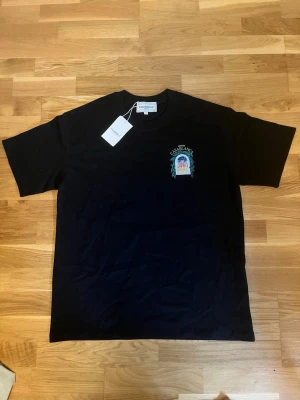 Svart t-shirt från Casablanca - Snygg svart t-shirt från Casablanca med tryck på bröstet som föreställer ett fönster med gröna blad och texten 'Avenida Casablanca'. Klassisk passform och rund hals. Perfekt för dig som gillar stilrena plagg med unika detaljer.
