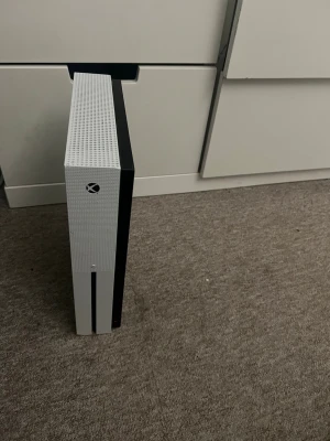 Xbox One S vit spelkonsol - Säljer en stilren Xbox One S i vit färg med svart detalj. Konsolen har en rektangulär form och är tillverkad i plast med ventilerad ovansida för bra kylning. Perfekt för gaming. Ingen kontroll följer med men sladdar följer med 