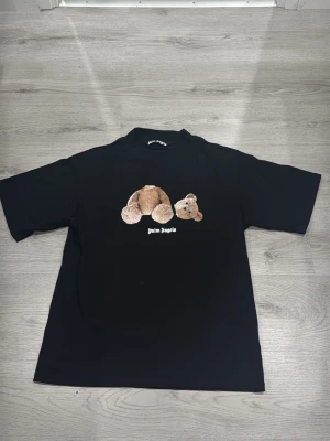 Svart Palm Angels t-shirt med björntryck - Svart t-shirt från Palm Angels med ikoniskt björntryck på bröstet och logga i vitt. T-shirten har en klassisk passform och korta ärmar. Perfekt för dig som vill ha en streetwear-look med edge.
