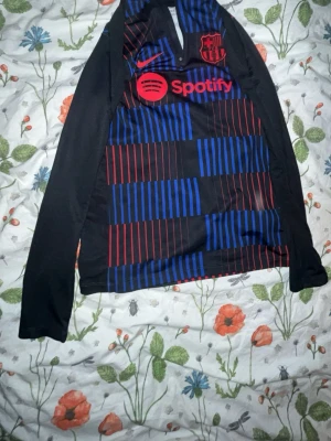 Barcelona långärmad träningströja - Snygg långärmad träningströja från FC Barcelona med svart bas och grafiskt mönster i blått och rött. Tröjan har klubbmärke och Nike-logga på bröstet samt Spotify som sponsor. Perfekt för fotbollsträning eller chill. pris går o diskutera 