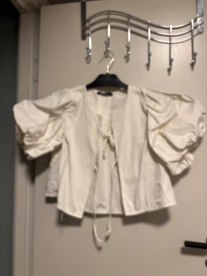 Vit blus med puffärmar från Gina Tricot - Superfin vit blus från Gina Tricot med puffiga trekvartsärmar och knytning framtill. Blusen har en luftig passform och är gjord i ett lätt tyg som känns fräscht och trendigt. Perfekt att styla med jeans eller kjol för en cool look.