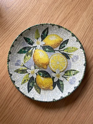Assiett Majas cottage - Tallrik från Majas cottage, mosaikmotiv med citroner. Köptes för 195kr säljes för 80kr. Använd fåtal gånger i väldigt fint skick. Storlek 21x2,5cm. Tål mikro och diskmaskin. 