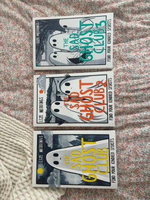 The Sad Ghost Club 1-3 av Lize Meddings - Säljer bokserien The Sad Ghost Club 1, 2 och 3 av Lize Meddings. Omslagen är vita med illustrationer av spöken och färgglada titlar i gult, orange och grönt. Perfekt för dig som gillar grafiska romaner och mysiga berättelser om vänskap och känslor.