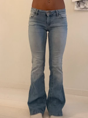 Ljusblå bootcut jeans - Säljer ett par ljusblå bootcut jeans med klassisk femficksmodell och normalhög midja. Jeansen har utsvängda ben och är tillverkade i mjukt denimtyg med lite stretch för skön passform. Perfekta för en trendig och avslappnad look.