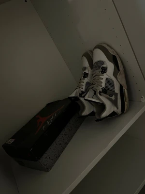 Vita och svarta sneakers Air Jordan - Snygga vita och svarta Air Jordan sneakers med meshdetaljer och grå inslag. Klassisk siluett med högt skaft och tydliga loggor på plösen. Skorna har en robust sula och cool design som sticker ut.