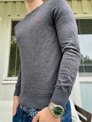 Grå stickad tröja från Morris - En riktigt snygg stickad tröja fån Morris🙌 Tröjan är i en extremt snygg mörkgrå och orange färg🤩 Extremt bra skick, inga som helst tecken på användning🤝  En av de skönaste materialen jag burit, 100% merinoull - kyler under sommaren och värmer under vintern❄️🤩. Rekommenderar denna starkt, ett nyckelplagg i garderoben🙌 Enda anledningen till att jag säljer den är att jag vuxit ur den🙌 Stl xs, längd från axel: 58cm