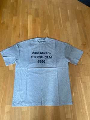 Acne Studios Tröja grå  - Säljer en snygg Acne Studios T-shirt i grå färg med det klassiska “Acne Studios STOCKHOLM 1996”-trycket framtill.  👕 Endast provad på – aldrig använd ✨ Nyskick 🎨 Gråmelerad 🖤 Stilren Acne Studios-design 📏 Storlek: M  T-shirten är i princip som ny och har inga märken, fläckar eller slitage. Perfekt som vardagsplagg och passar enkelt till både jeans och andra outfits.  📦 Skickas väl emballerad. Hör gärna av dig om du har frågor eller vill ha fler bilder!