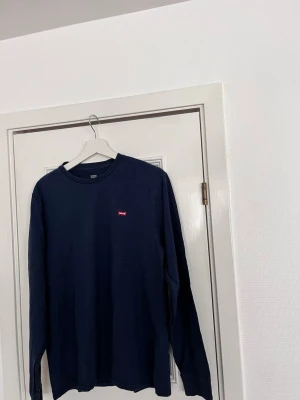 Mörkblå långärmad  Levi's - Mörkblå långärmad topp från Levi's med rund halsringning och liten röd logotyp på bröstet. Tillverkad i mjuk bomull som känns skön mot huden. Perfekt till jeans eller kjol för en clean och enkel look.