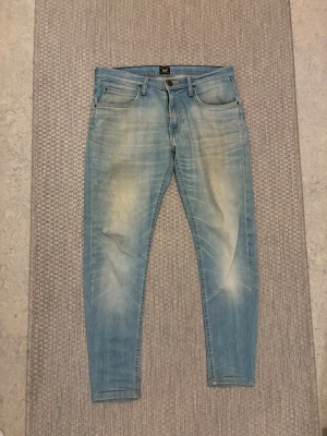 Ljusblå skinny jeans från Lee - Säljer ett par ljusblå skinny jeans från Lee med slitna detaljer och snygg tvätt. Klassisk femficksmodell med dragkedja och knapp. Perfekta för dig som gillar en avslappnad men trendig stil.