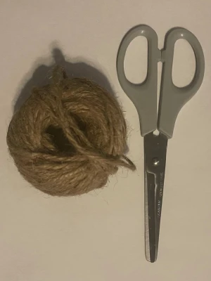 Sax och snöre i naturfärg - Ett set med en grå sax i plast och metall samt ett nystan naturfärgat snöre av jute. Perfekt för pyssel, paketinslagning eller andra kreativa projekt. Saxen har rundade handtag och snöret är grovt tvinnat.