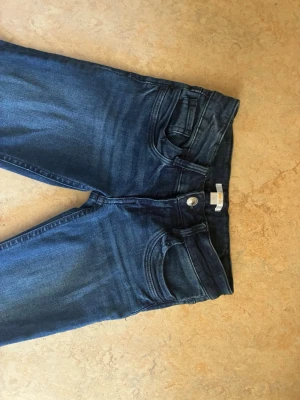 Mörkblå bootcut jeans - Snygga lågmidjade jeans med utsvängda ben och klassisk femficksmodell. Jeansen har en knapp och dragkedja framtill samt subtila slitningar för en trendig look. Tillverkade i ett mjukt denimtyg som sitter skönt hela dagen. Skriv för frågor eller fler bilder!💕