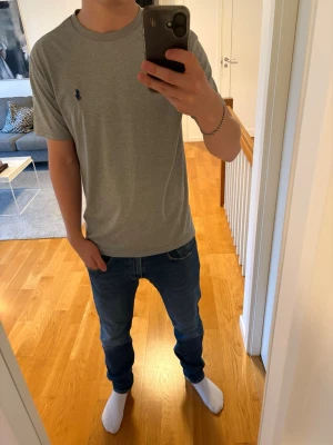 Grå t-shirt från Polo Ralph Lauren - Snygg grå t-shirt från Polo Ralph Lauren med klassisk passform och liten mörkblå logga broderad på bröstet. Tillverkad i mjuk bomull och har rund halsringning samt korta ärmar. Perfekt basplagg till garderoben.