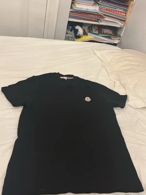 Svart t-shirt med logga - En stilren svart t-shirt med rund hals och korta ärmar. På bröstet sitter en liten broderad logga som ger en clean och exklusiv känsla. Perfekt till jeans eller shorts för en enkel men snygg look.