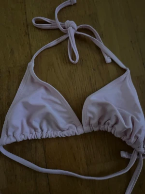Ljusrosa trekantsbikinitopp XS - Söt ljusrosa trekantsbikinitopp med knyt i nacken och ryggen. Enkel och stilren design som passar perfekt till sommaren. Tillverkad i mjukt syntetmaterial för skön passform.