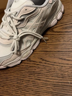Vit beiga acics skor  - Snygga vita sneakers med detaljer i mesh och mocka samt inslag av ljusgrått. Skorna har en chunky sula och klassisk snörning. Perfekta för dig som gillar sportig och clean stil.
