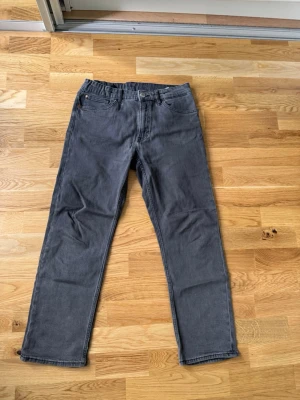 Grå raka jeans från H&M - Snygga grå jeans från H&M med rak passform och klassisk femficksdesign. Jeansen har normal midja och är tillverkade i ett mjukt bomullsmaterial med lite stretch för extra komfort. Perfekta till en avslappnad stil.