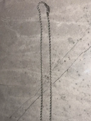 Tunt silverfärgat kedjehalsband - Säljer ett stilrent halsband i silverfärg med tvinnad kedja. Halsbandet har en enkel och klassisk design som passar till många olika stilar. Perfekt för dig som gillar minimalistiska accessoarer.