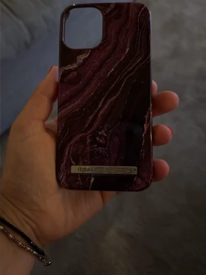 Mörklila marmormönstrat mobilskal iPhone 12 mini - Snyggt mobilskal från iDeal of Sweden med mörklila och svart marmormönster. Skalet har en glansig finish och en metallbricka med loggan längst ner. Tillverkat i hårdplast och designat för att skydda mobilen med stil.