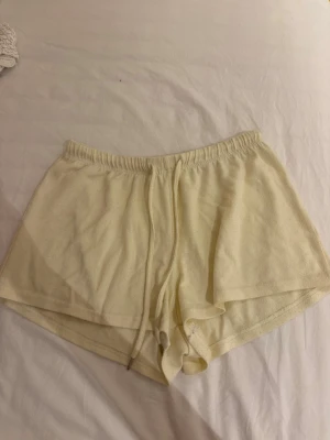 Ljusgula mjuka shorts med snörning - Säljer ett par ljusgula shorts i mjukt frottématerial. De har elastisk midja och snörning framtill för extra komfort. Perfekta för lata dagar hemma eller sommarens varma kvällar.