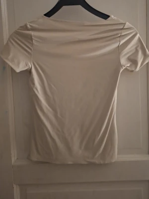 Beige topp med fyrkantig ringning - Säljer en stilren beige topp med korta ärmar och fyrkantig ringning. Toppen har en enkel och clean design som passar till det mesta. Materialet känns mjukt och stretchigt, perfekt för en avslappnad look.