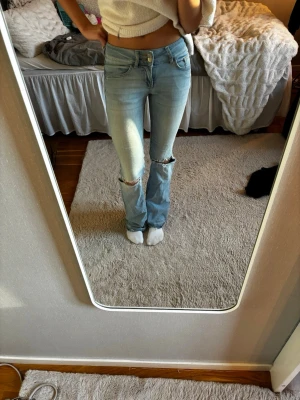 Ljusblå bootcut jeans med slitningar och fickor med knappar - De är i bra skick men man kan se att de är använda då de är ganska slitna vid fötterna.
