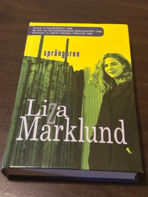 Sprängaren av Liza Marklund - En spännande thriller av Liza Marklund som utspelar sig i Stockholm. Boken har ett omslag i gult och grönt med ett foto av en kvinna och stadsmiljö. Handlingen kretsar kring journalisten Annika Bengtzon och ett bombdåd inför OS. Utgiven av Ordupplaget.